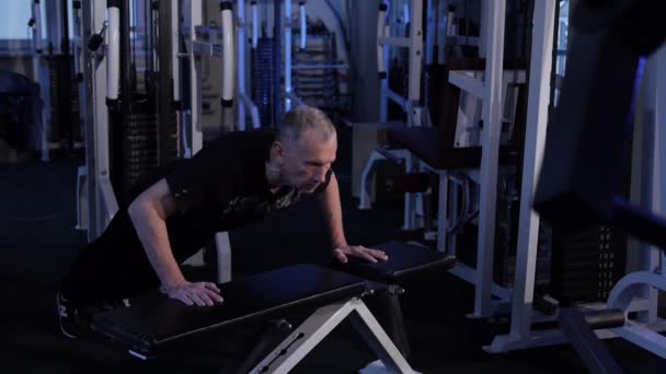 Gammal man skjuter sig själv utanför bänken på gymmet. Kopiera mellanslag. sidovy — Stockvideo