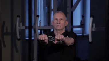 Yaş bir adam spor salonunda parmaklar için ortak jimnastik yapar. Yumruğunu sıkıyor ve amcana vuruyor, kollarını önünde. Kopyalama alanı
