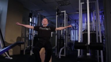 Yaş bir adam spor salonunda parmaklar için ortak jimnastik yapar. Sıkma ve yumruk, kollar sol ve sağ uzatılmış. Kopyalama alanı