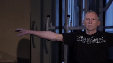 Yaş bir adam spor salonunda parmaklar için ortak jimnastik yapar. Sıkma ve yumruk, kollar sol ve sağ uzatılmış. Kopyalama alanı
