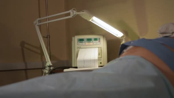 Mujeres embarazadas estómago en un sofá médico y un monitor cardíaco.cardiograma en papel — Vídeo de stock