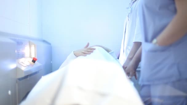 Η έγκυος γυναίκα βρίσκεται σε ένα φορείο σε ένα ασανσέρ σε μια κλινική. Της χαϊδεύει την κοιλιά με το χέρι της. Οι νοσοκόμες στέκονται κοντά — Αρχείο Βίντεο