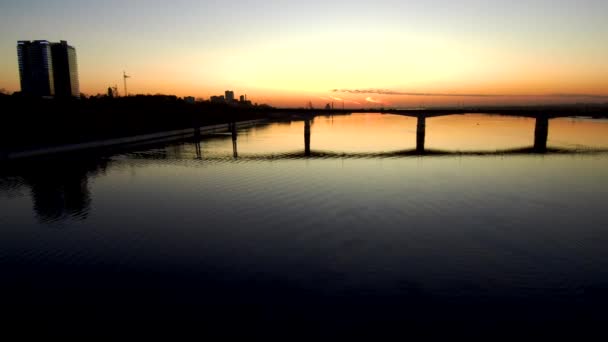 Vista aérea oscura del puente a través de un amplio río al atardecer, la puesta de sol se refleja en el agua.4k.Espacio de copia — Vídeo de stock