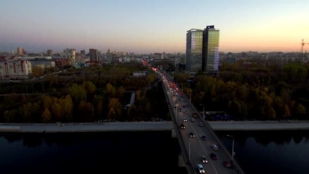 Letecký pohled na aktivní provoz na mostě přes velkou řeku večer, viditelná světla z aut. Na pozadí-město, podzimní stromy. 4k. místo pro kopírování — Stock video