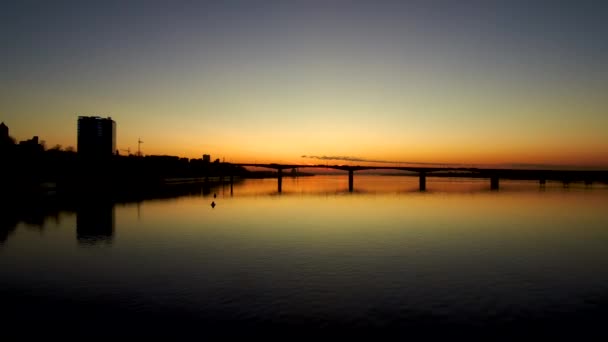 Oscura Vista aérea del Puente a través de un amplio río al atardecer en la gran ciudad.La puesta de sol se refleja en el agua.4k.Espacio de copia — Vídeo de stock