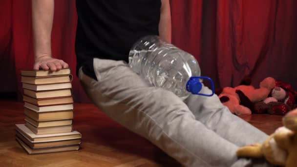 El hombre realiza flexiones usando dos pilas de libros y una botella de agua . — Vídeo de stock