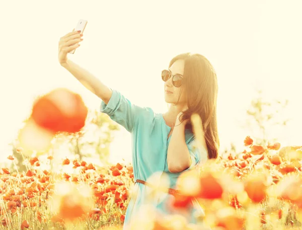 ポピー草原の日当たりの良い夏の日にスマート フォンで Selfie を取ってサングラスで美しい若い女性 — ストック写真