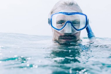 Deniz yüzeyi açık, kameraya bakarak yukarıda maskeli giyen genç adam freediver portresi.