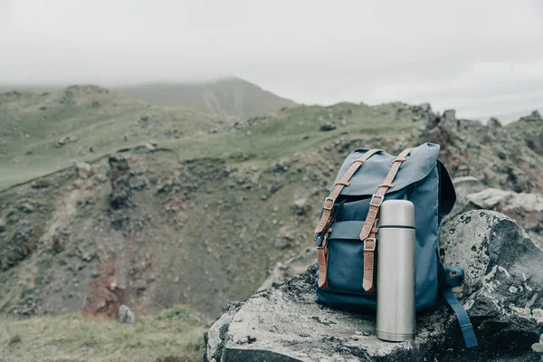 Backpack and thermos on stone in the mountains outdoor, concept of wanderlust.