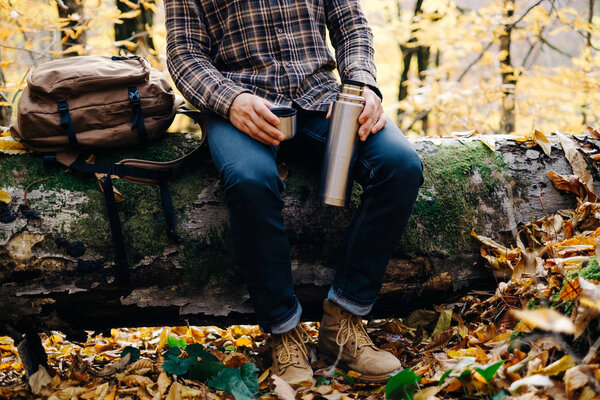 Man sitting on fallen tree trunk with thermos.