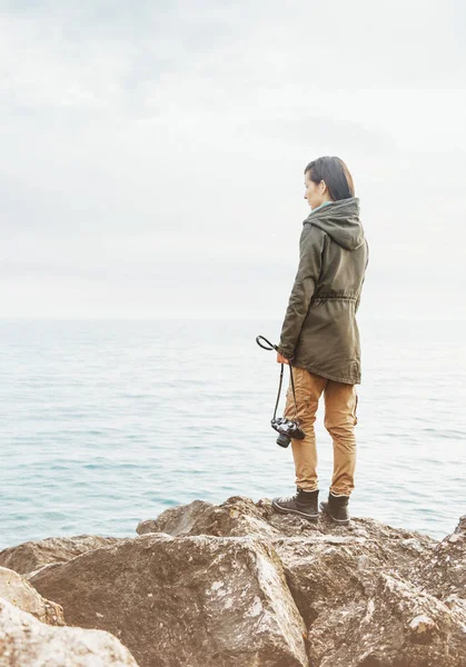 Podróżnik kobieta stojąc na wybrzeżu z aparatu fotograficznego. — Zdjęcie stockowe
