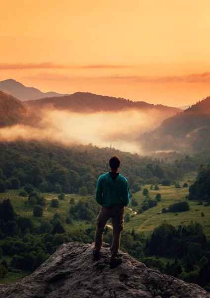 Reisender Mann steht bei Sonnenuntergang auf Gipfel der Klippe in den Bergen. — Stockfoto