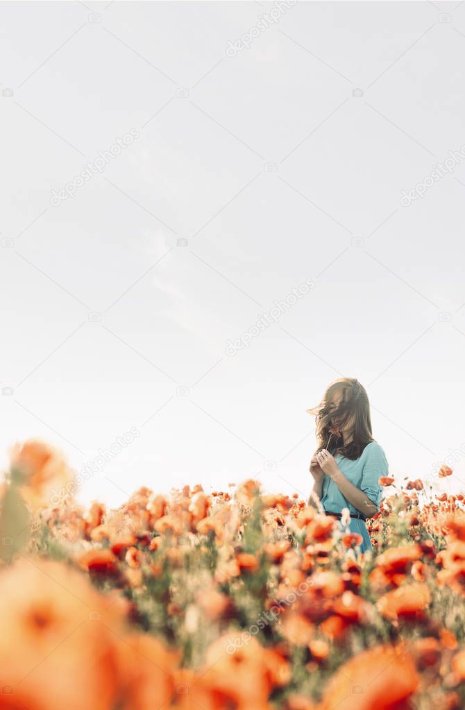 Romantic young woman walking in poppy flowers meadow. 