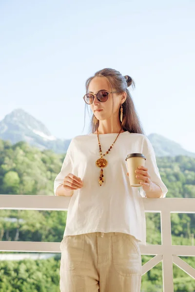 Όμορφη γυναίκα που αναπαύεται με φλιτζάνι καφέ στο μπαλκόνι μπροστά o — Φωτογραφία Αρχείου