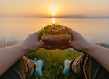 Woman with tasty burger by the sea, point of view.  clipart