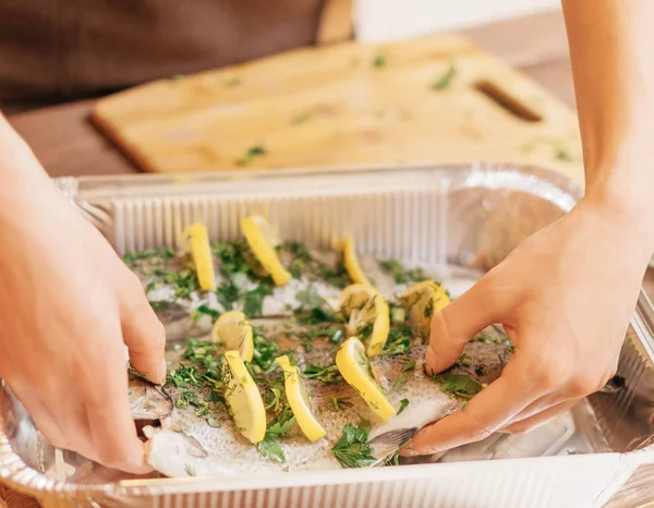Kvinna sätta rå fisk öring i bakning skålen i köket. — Stockfoto
