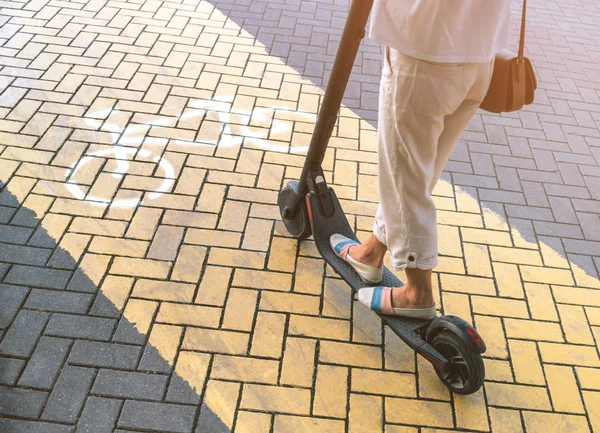 Mulher montando uma scooter elétrica no caminho do ciclo, vista das pernas . — Fotografia de Stock