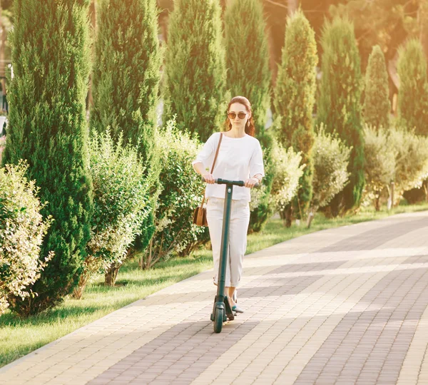 Mujer joven montando un scooter eléctrico en el parque de verano . —  Fotos de Stock