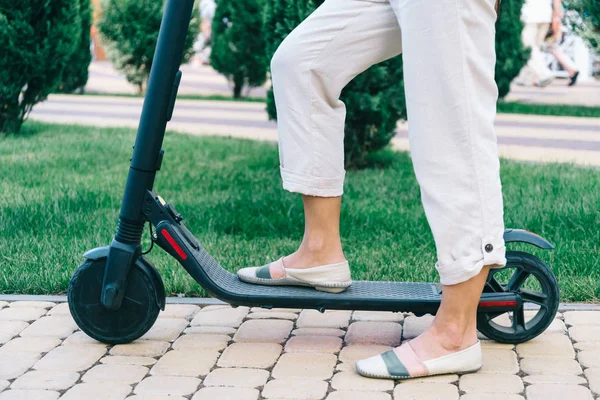 Mulher montando uma scooter elétrica no parque, vista das pernas . — Fotografia de Stock