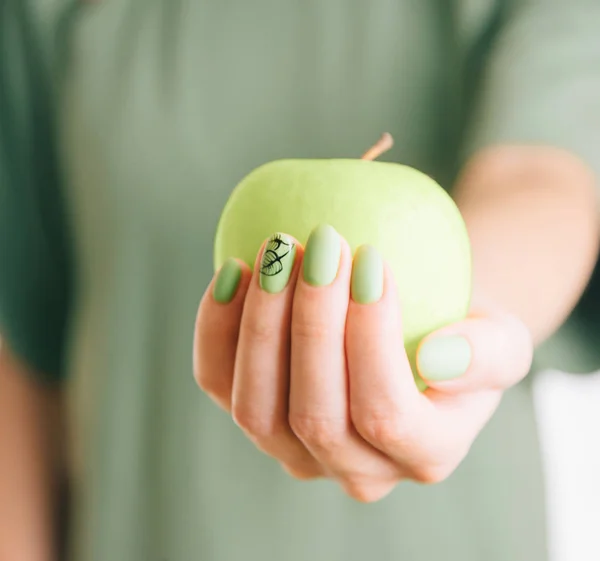 Female hand with green manicure holding an apple.