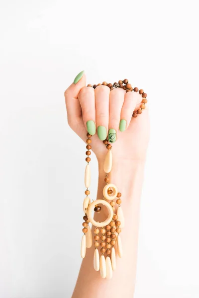 Female hand with green manicure holding wooden necklace. — Stock Photo, Image
