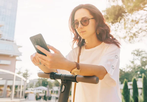 Donna moderna utilizzando smartphone mentre in piedi con uno sc elettrico — Foto Stock