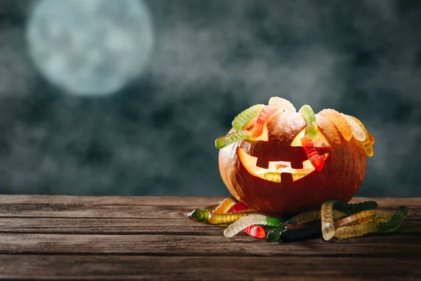 Pumpkin with colorful candies in form of worms in Halloween nigh — Stock Photo, Image