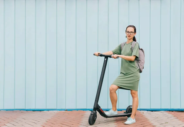 Menina em vestido verde de pé com e-scooter na rua . — Fotografia de Stock