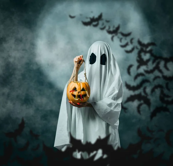 White ghost holding a carved pumpkin with candies in Halloween n — Stock Photo, Image