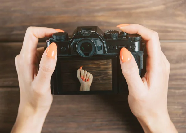 Woman holding camera with photo of hand with orange manicure on — Stock Photo, Image