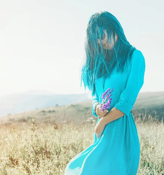 在夏天的草地上 身穿蓝色衣服 头戴野花束的年轻女子走在路上 — 图库照片