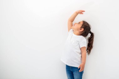 Beyaz duvarın yanında boyunu ölçen küçük kız..