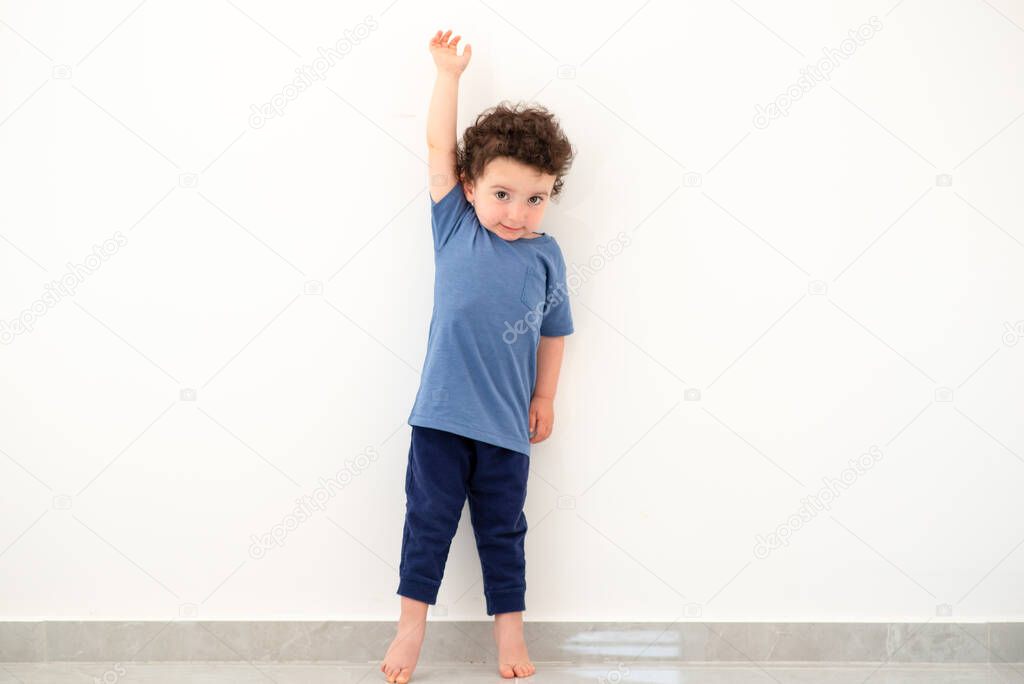 Little boy measuring height near white wall.