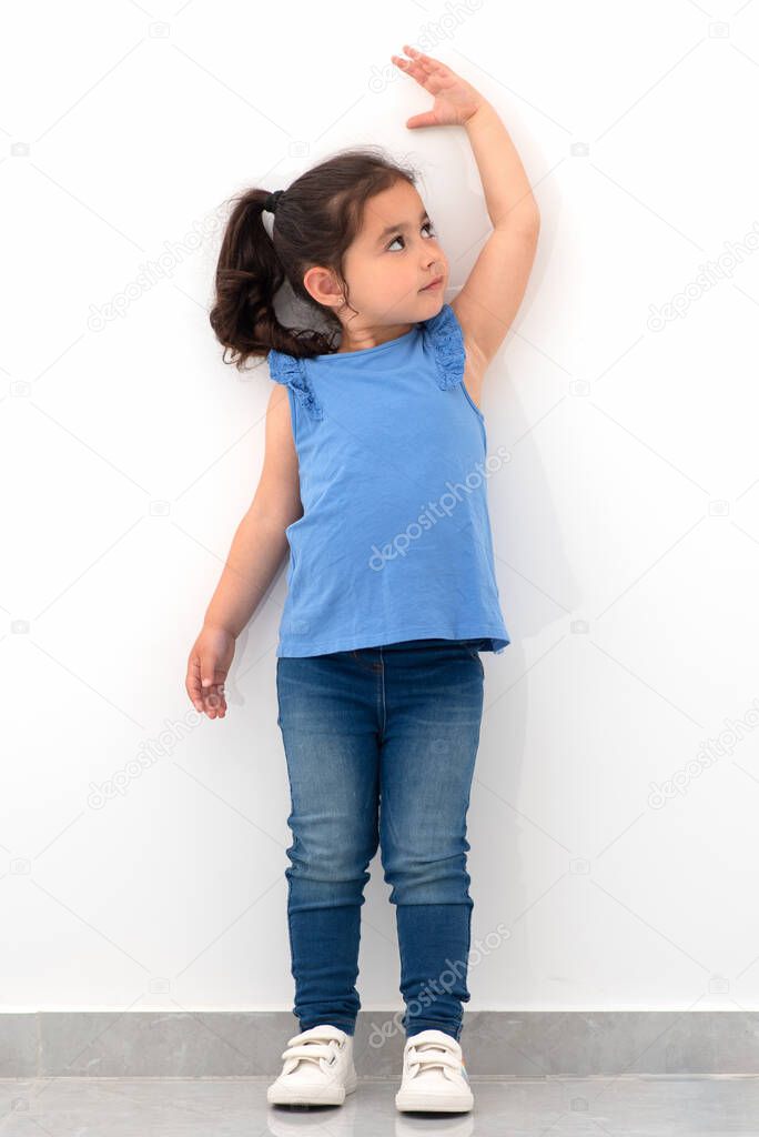 Little girl measuring height near white wall.
