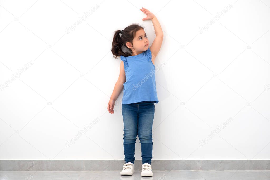 Little girl measuring height near white wall.