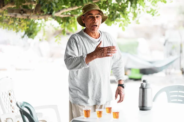Арабський старший чоловік розмовляє і жестикулює біля столу традиційним чаєм.. — стокове фото