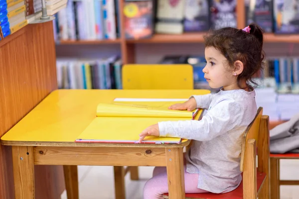 Маленька дівчинка перед книжками. Симпатичний молодий Тоддлер сидить на стільці біля столу і читання книги . — стокове фото
