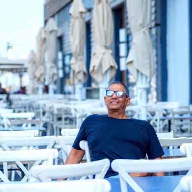 Kafesinde oturan kıdemli bir kafenin sahibinin portresi. Kahve dükkanındaki turist kameraya gülümsüyor..