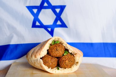 İsrail bayraklı arka planında, tahta masada pide köfteler. Falafel İsrail mutfağında ikonik bir rol oynuyor ve yaygın olarak ülkenin ulusal yemeği olarak kabul ediliyor..