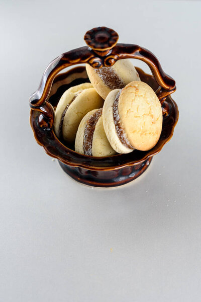 Вкусное аргентинское печенье с кремом тупой де Лече крупным планом в коричневой керамической вазе. Белый ванильный макарон на белом фоне. Французский деликатный десерт на завтрак.