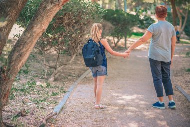 Büyükanne ve öğrenci çocuk okula giderken el ele tutuşuyor. Okul çantalı küçük kız ya da büyükannesiyle okula yürüyen çantalı kız. Yaşlı ebeveyn ve kız, büyükanne ve torun, dikiz aynası..