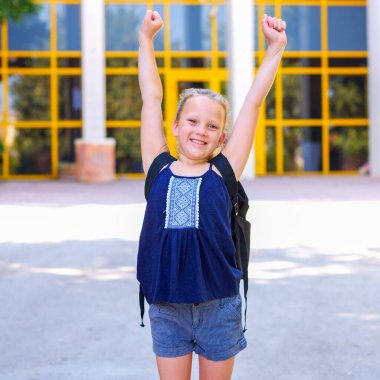 Çocuk eğleniyor. Mutlu küçük kız ellerini havaya kaldırıyor. Hayatın tadını çıkarıyorum. Güneşli, sağlıklı yaşam tarzı, başarılı öğrenme. Öğrenciler Neşeli Mutluluk Konsepti.
