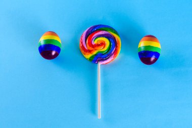 Lgbt ailesi. Lgbt bayrağı renginde yumurta ve mavi arka planda gökkuşağı lolipopu. Eşcinsel çiftlerin çocuk evlat edinmesi ve büyütmesi için yaratıcı bir fikir. Gay yaz partisi.