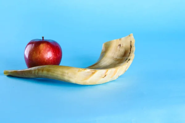 Rosh Ha Shana - Jewish new year composition of an red apple and Shofar horn for Rosh Hashanah on blue background.Jews dip a slice of apple in honey to express hopes for a sweet and fruitful year.