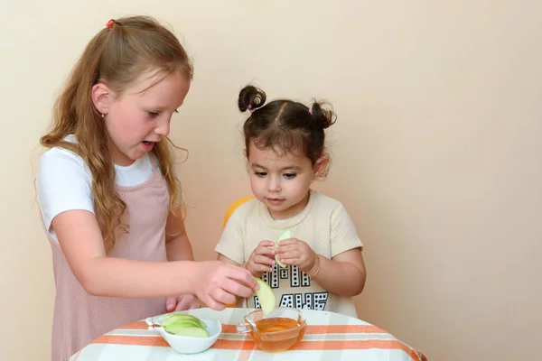 Kapalı alanda elma yiyen iki komik küçük kızın portresi. Yeni Yahudi Rosh HaShanah 'ın üzerine elma dilimleri bandıran Yahudi çocukları. Mutlu aile Rosh HaShana' yı kutluyor..