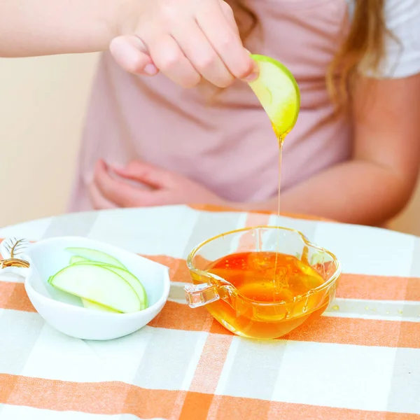 Close up of hands little girl eat apple with honey indoor. Jewish child dipping apple slices into honey on Rosh HaShanah the Jewish New Year.