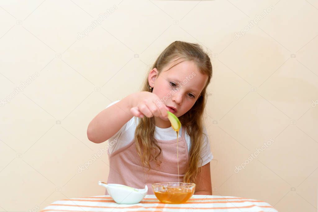 Close up portrait of funny lovely caucasian little girl eat apple with honey indoor. Jewish child dipping apple slices into honey on Rosh HaShanah the Jewish New Year.