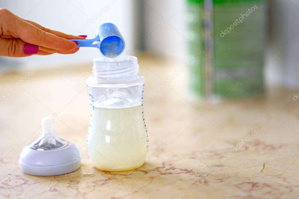 Preparation of mixture baby feeding on marble table background in morning kitchen. Happy moments, sunny day, mother prepares a baby formula feeding bottle with milk formula on table.