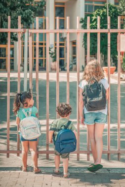 Genç bir kız ve erkek kardeş kapalı bir okul kapısında bekliyorlar. Çeşitli okul çocukları okula gidiyor..