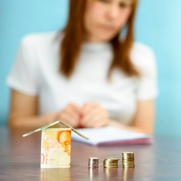 Middle age Woman With Model House from Israel Currencies new israeli shekel On wooden Table. Woman relaxing at home, building house from Israel 100 and 50 banknotes.Selective focus on money.